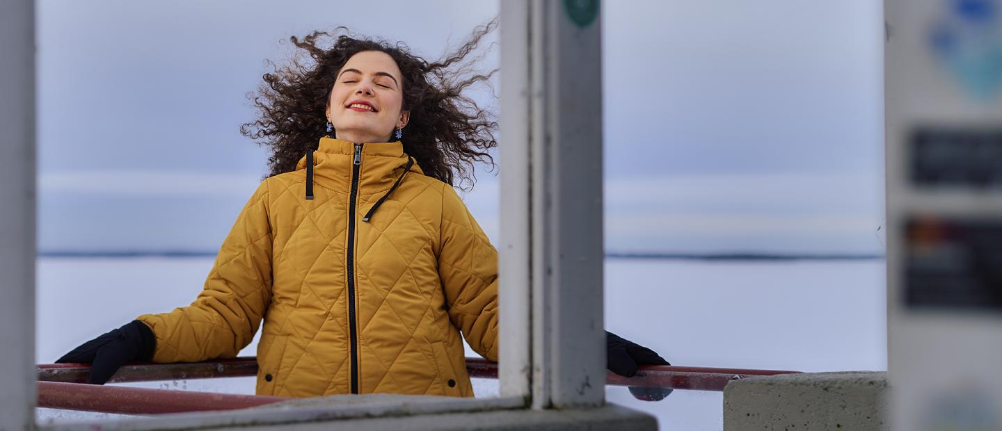 Tummahiuksinen nuori nainen hymyilee silmät suljettuina.