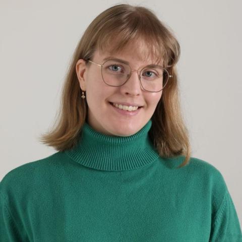 Profile picture of Sonja Palmo, a brown-haired smiling young woman with eyeglasses and a green turtle-neck sweater. 