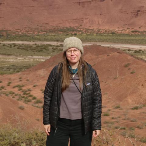 Woman in a beanie and black jacket standing in a desert canyon landscape.