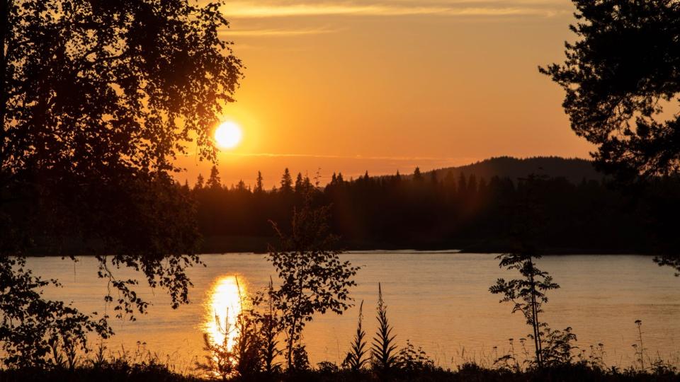Tornionjoki oranssin keskiyönauringon loisteessa, vaaramaisemaa näkyen toisella rannalla