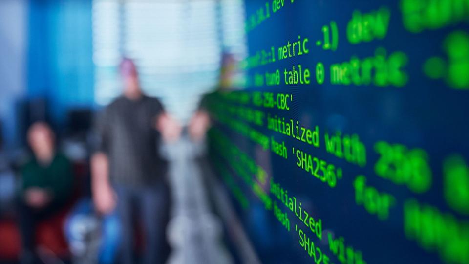 html code on a screen, people in the background