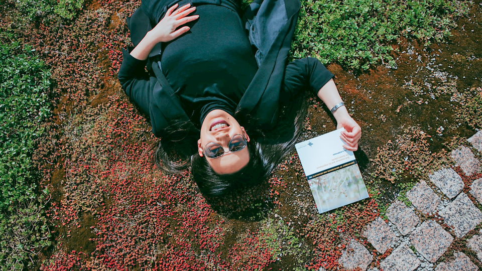 a scientist lying on a vegetation mat shows her thesis book