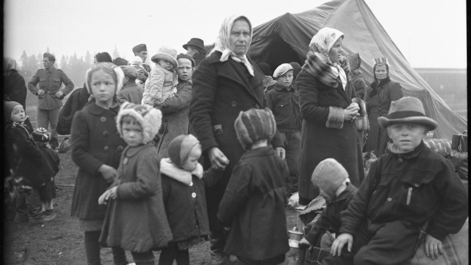 Lapsia ja aikuisia siirtymässä pois Lapin sodan jaloista, taustalla kota. Mustavalkoinen kuva vuodelta 1944.