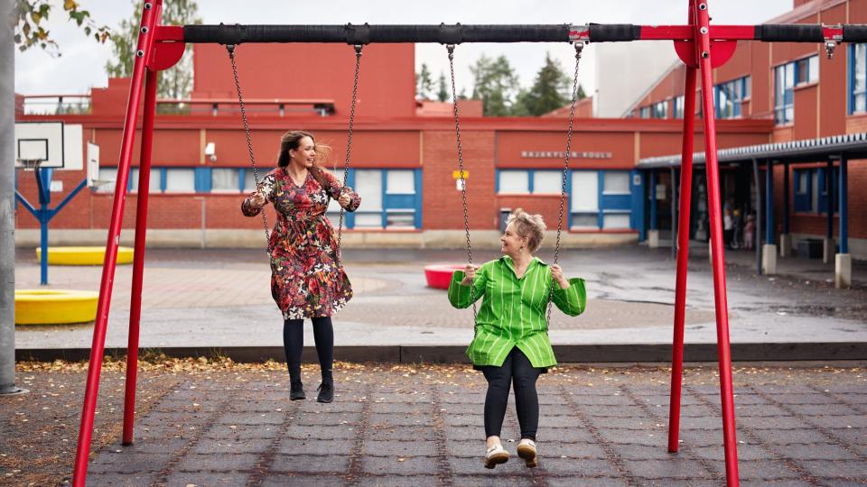 Satu-Maaria Toppinen ja Anu Uusikylä keinuvat koulun pihalla.