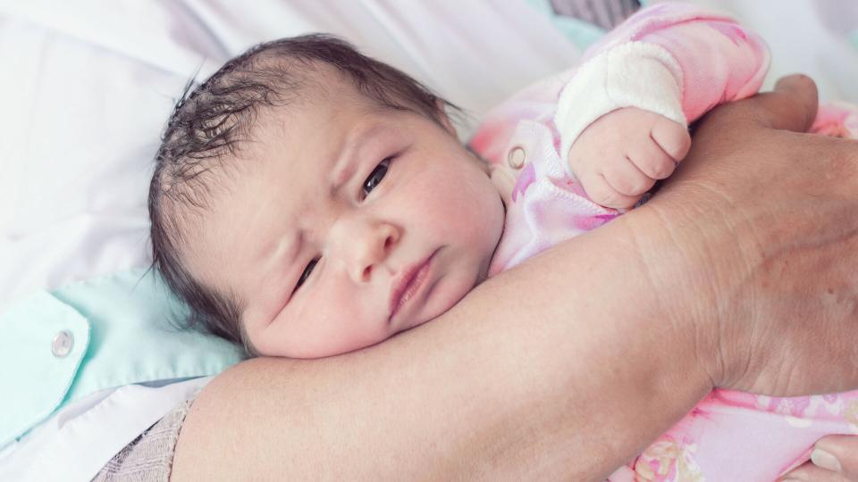 A newborn baby lying in the adult´s lap.
