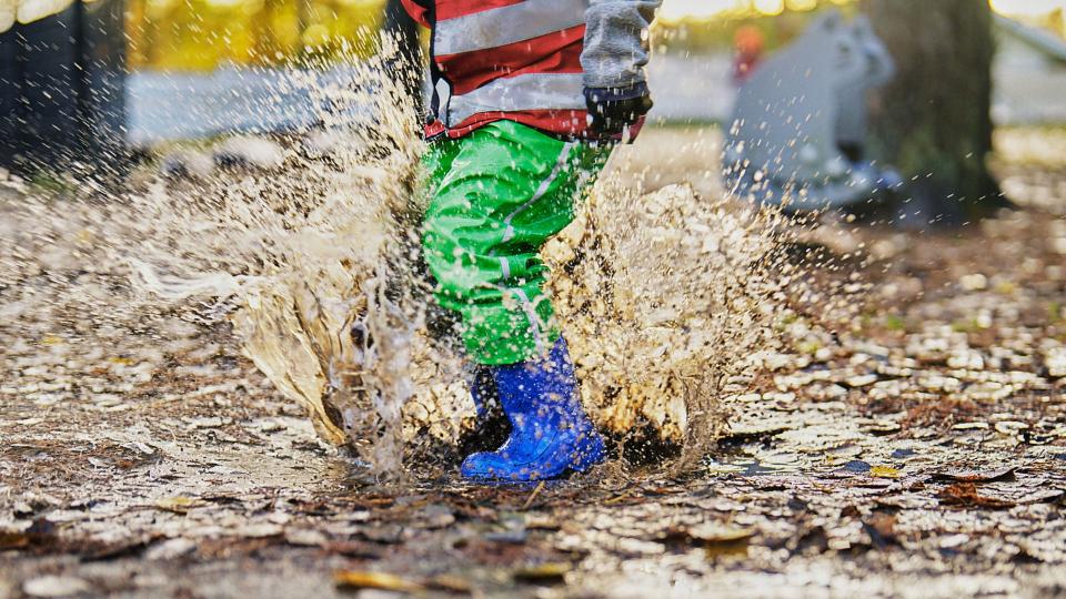 A child in colorful mud pants jumps in a puddle.