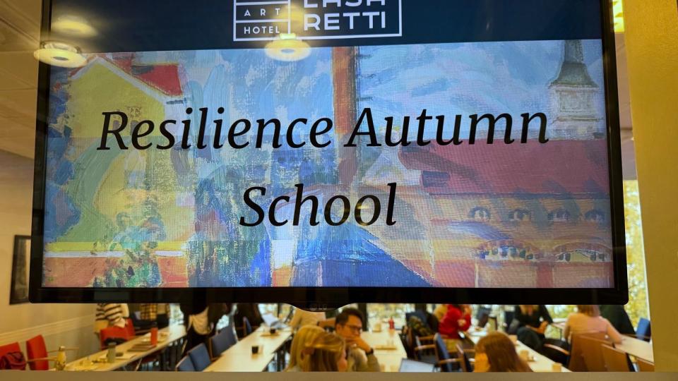 A sign that says Resilience Autumn school with people sitting in the classroom in the background