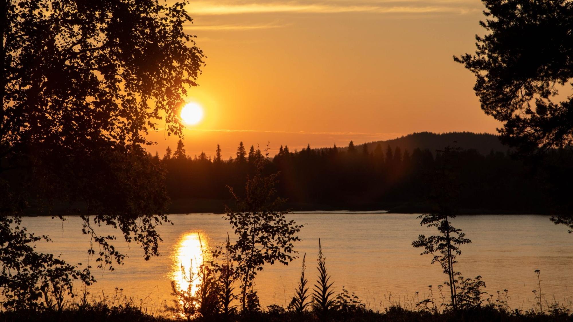 Tornionjoki oranssin keskiyönauringon loisteessa, vaaramaisemaa näkyen toisella rannalla
