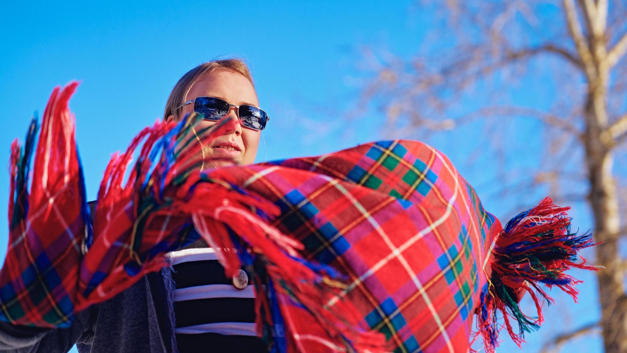 A person with sunglasses on with a traditional Sami scarf in movement in the front