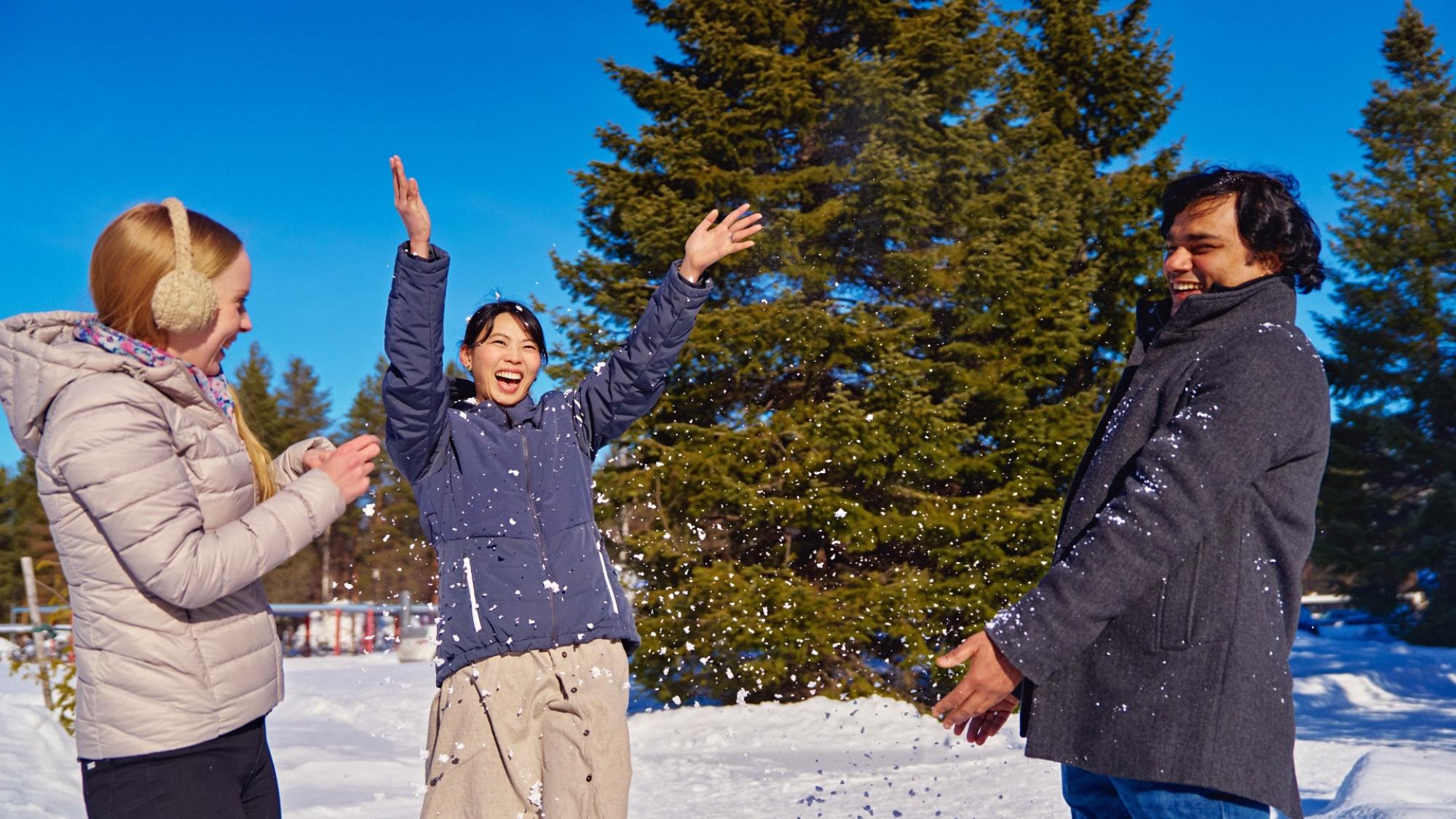 Three persons in sunny winter wearther throwing snow to the air and laughing