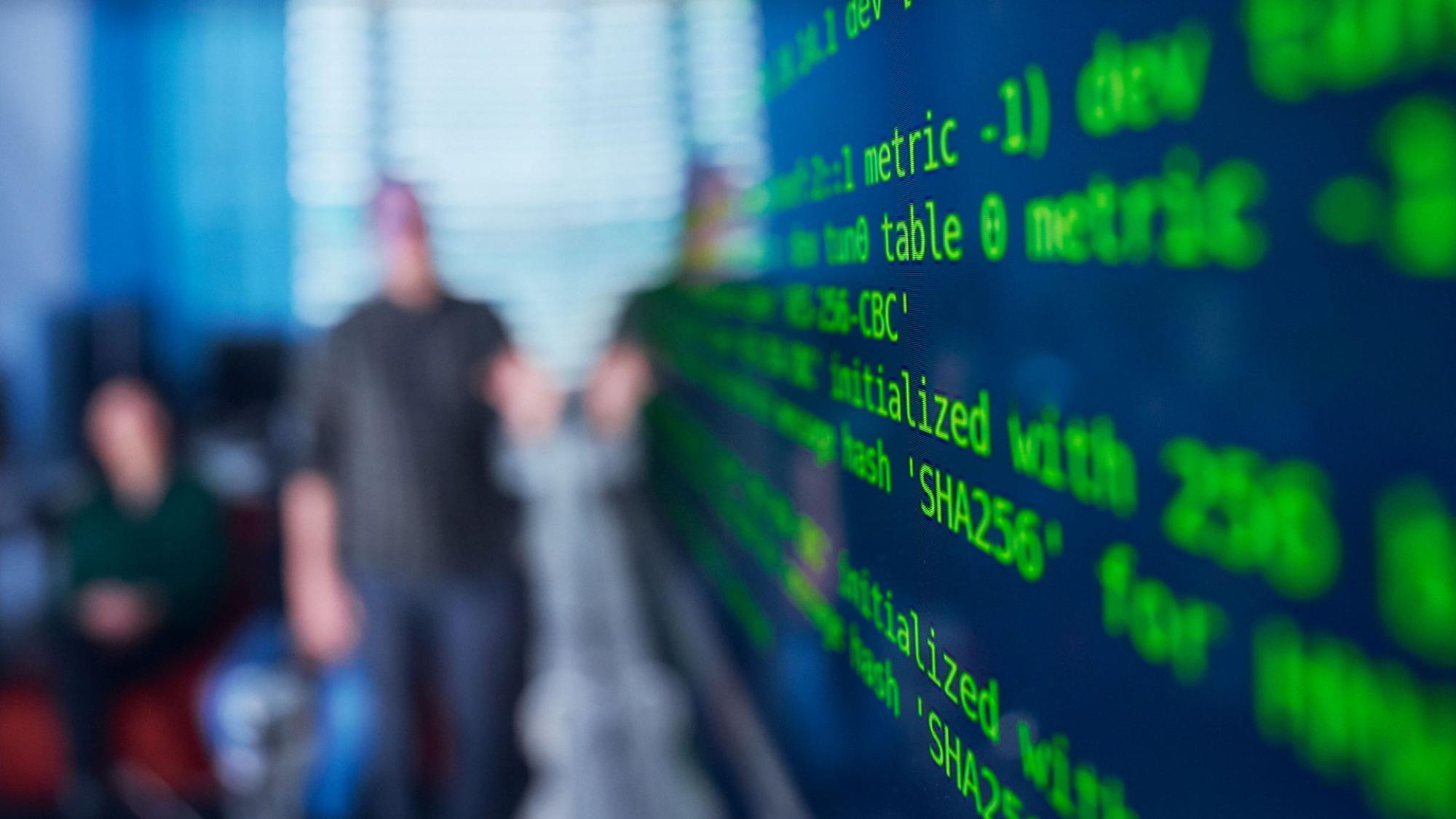 html code on a screen, people in the background