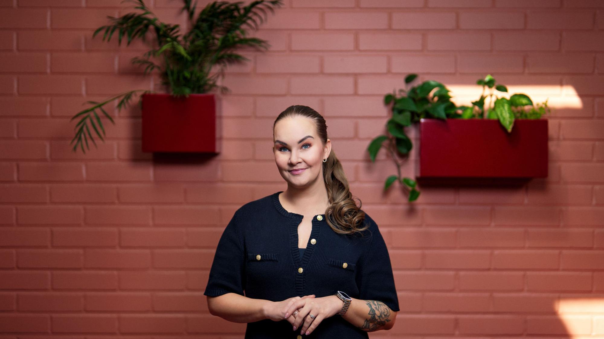 Kauppatieteiden alumni Jenni Ahokas seisoo punaisen seinän edessä.