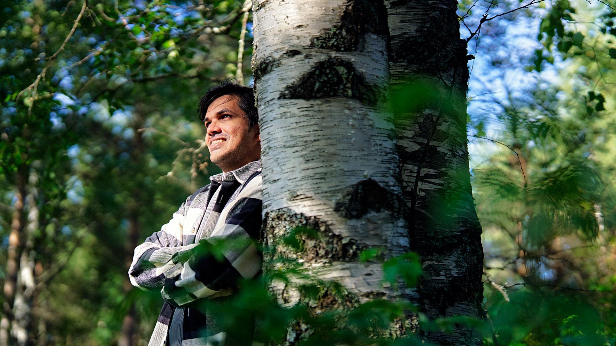 Sadeep Rathnayake hymyilee nojaillen koivuun metsässä.