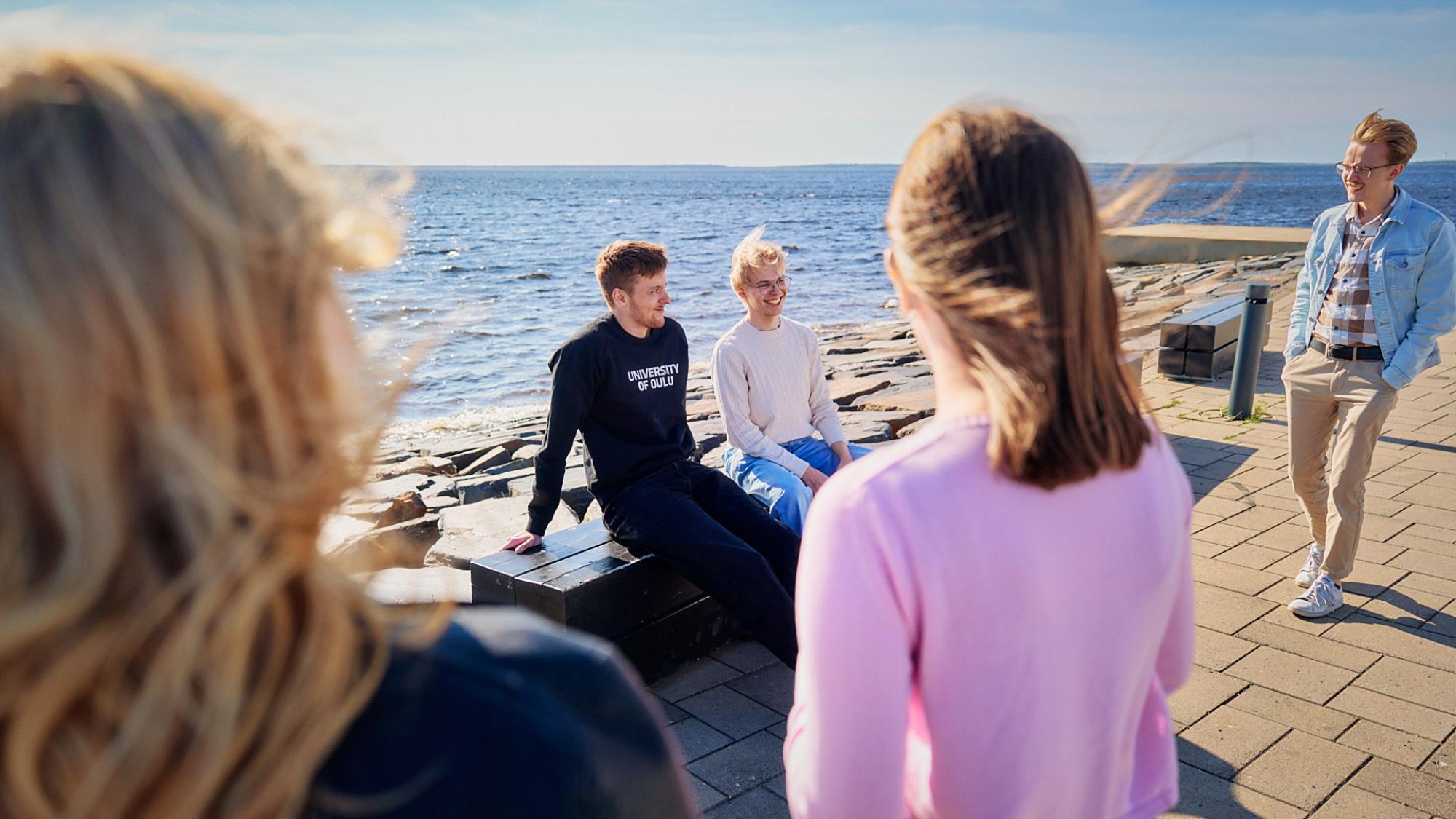 Opiskelijalähettiläitä meren äärellä. Aurinko paistaa ja yhdellä on päällään Oulun yliopiston collegepaita.