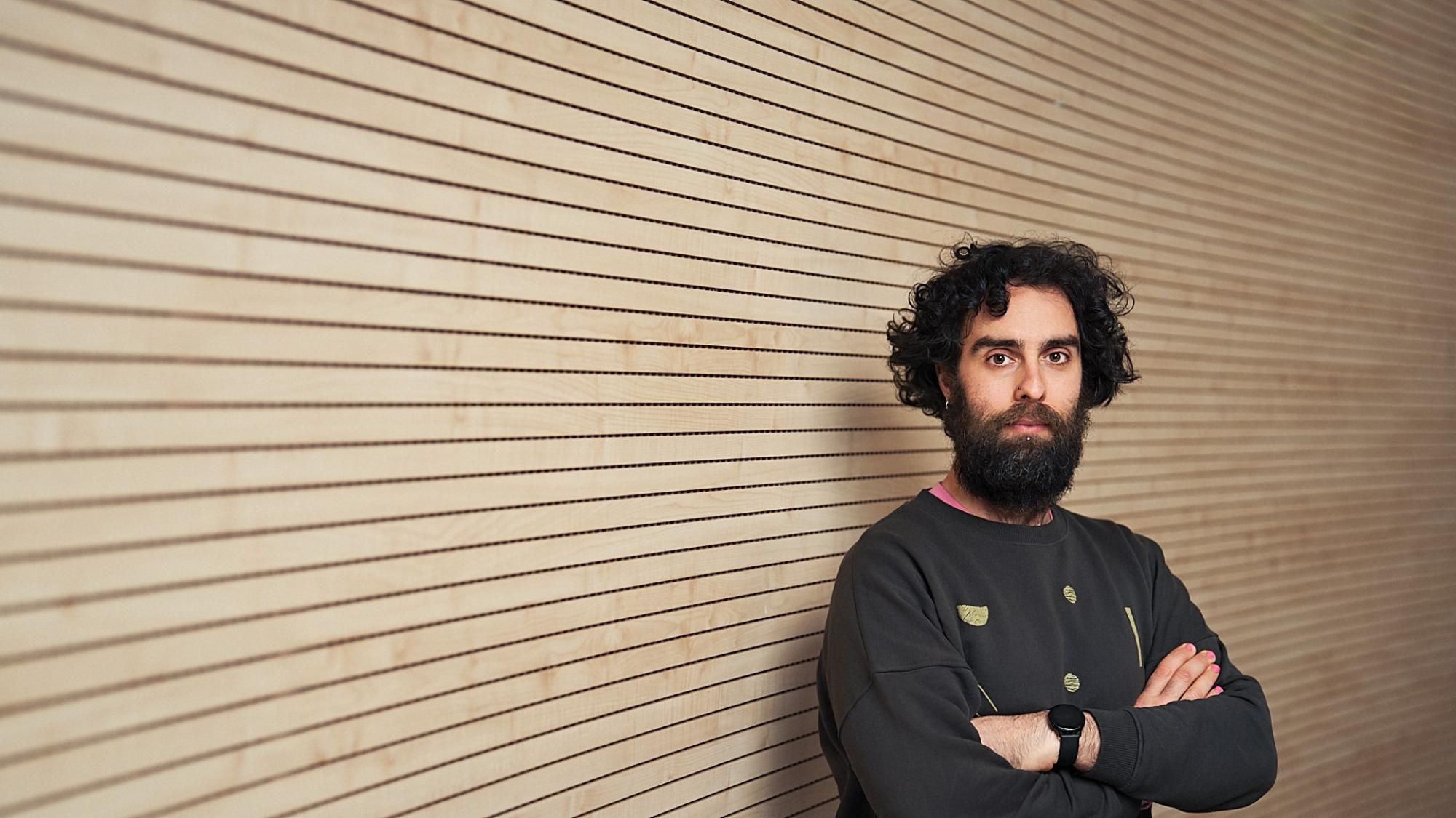 Researcher Jose A. Cañada stands with crossed arms in front of a wooden wall.