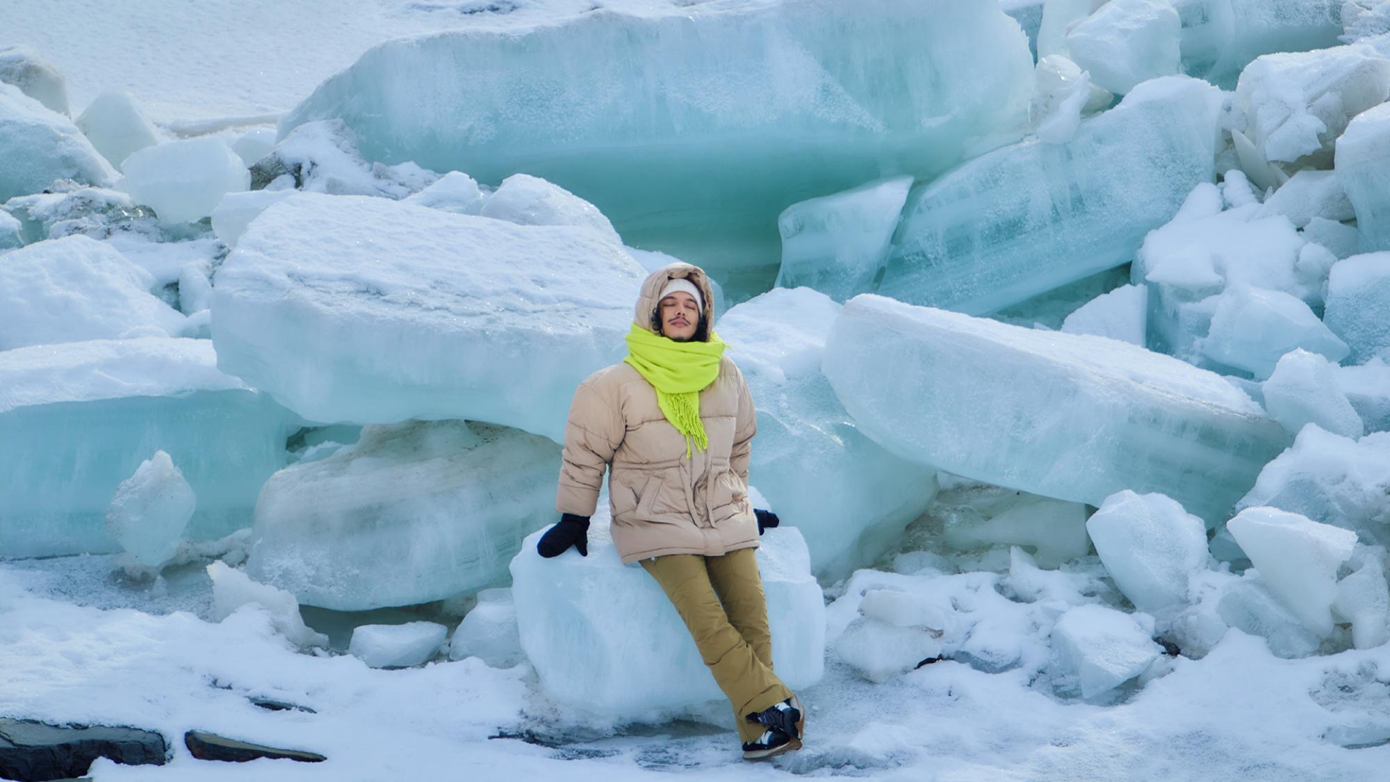 A young man with his eyes closed is surrounded by large blocks of ice.