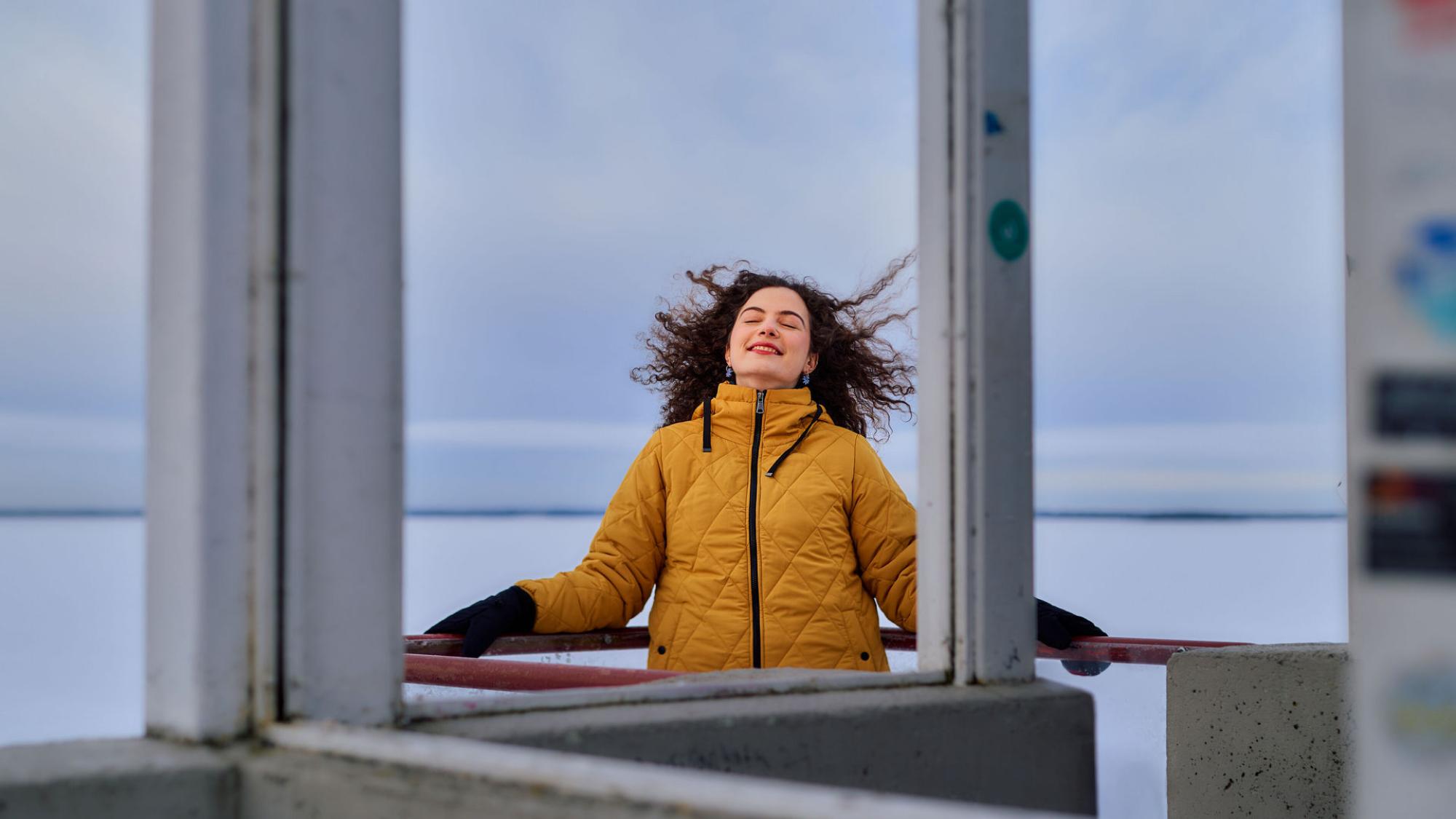 Iloinen nuori nainen ulkona talvisäässä taustallaan jäätynyt meri.