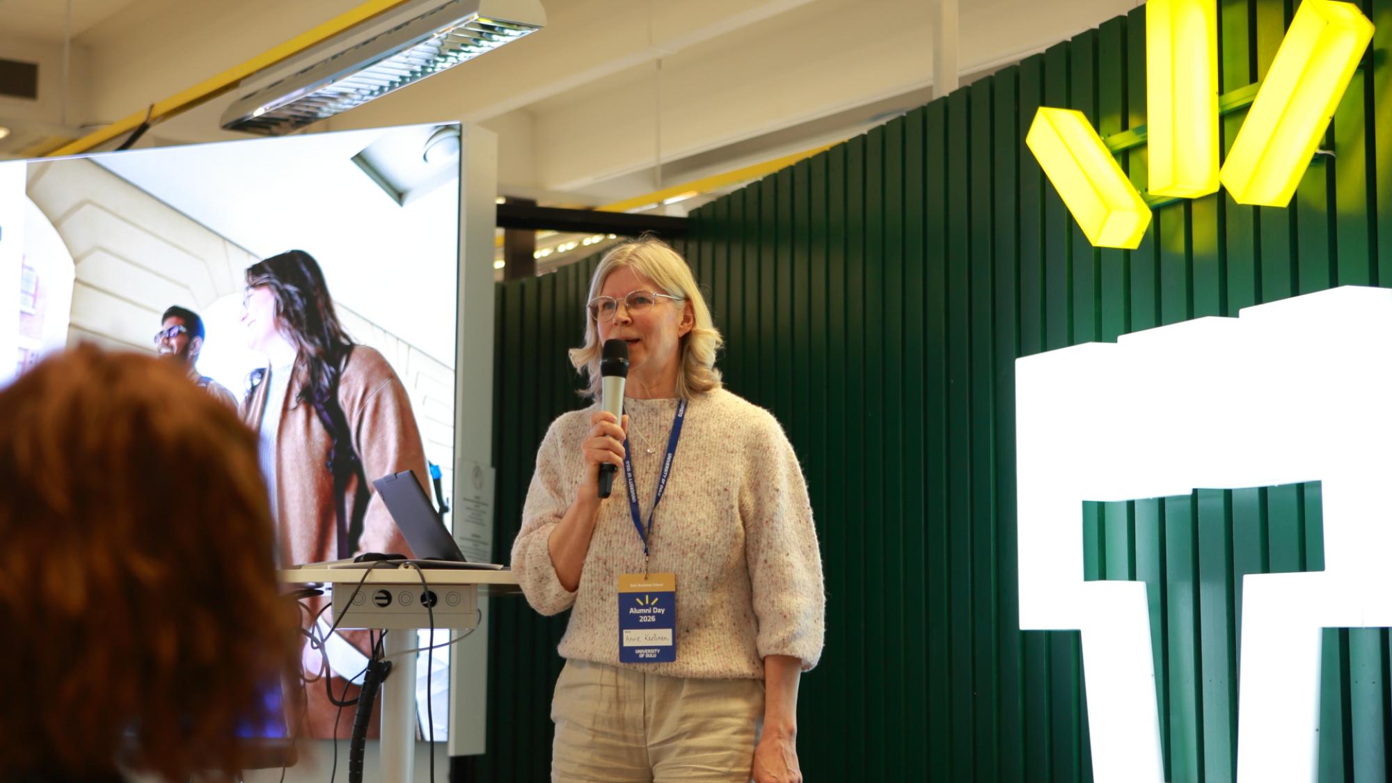 Anne Keränen speaking to a microphone in from of UniOulu logo.