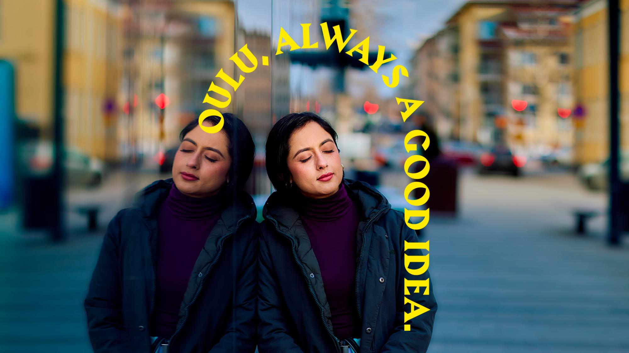 A woman wearing a winter jacket is leaning to a mirror wall. Her figure is reflected on the wall. Her eyes are closed. A text appears above her stating Oulu, always a good idea.