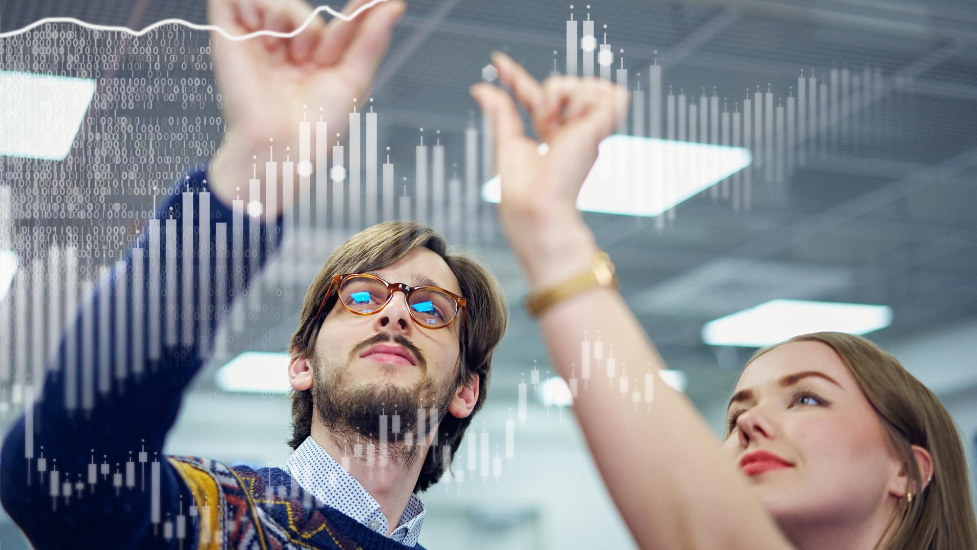 A young man with glasses and a young woman zooming graphic patterns of augmented reality in the air with their fingers
