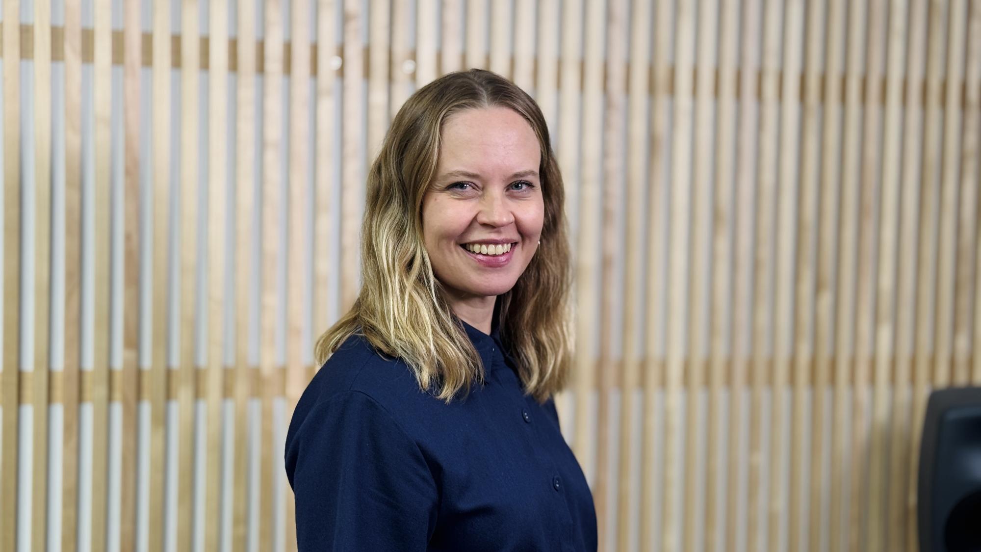 Niina Palmu in a portrait smiling with a wooden wall in the background.