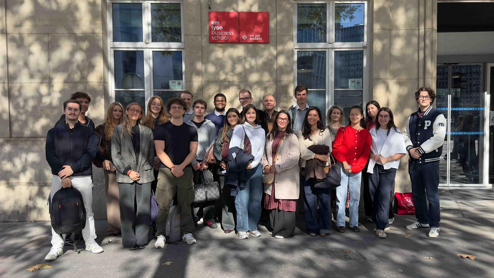 A group of 20 people standing in front of an building in a sunny weather.