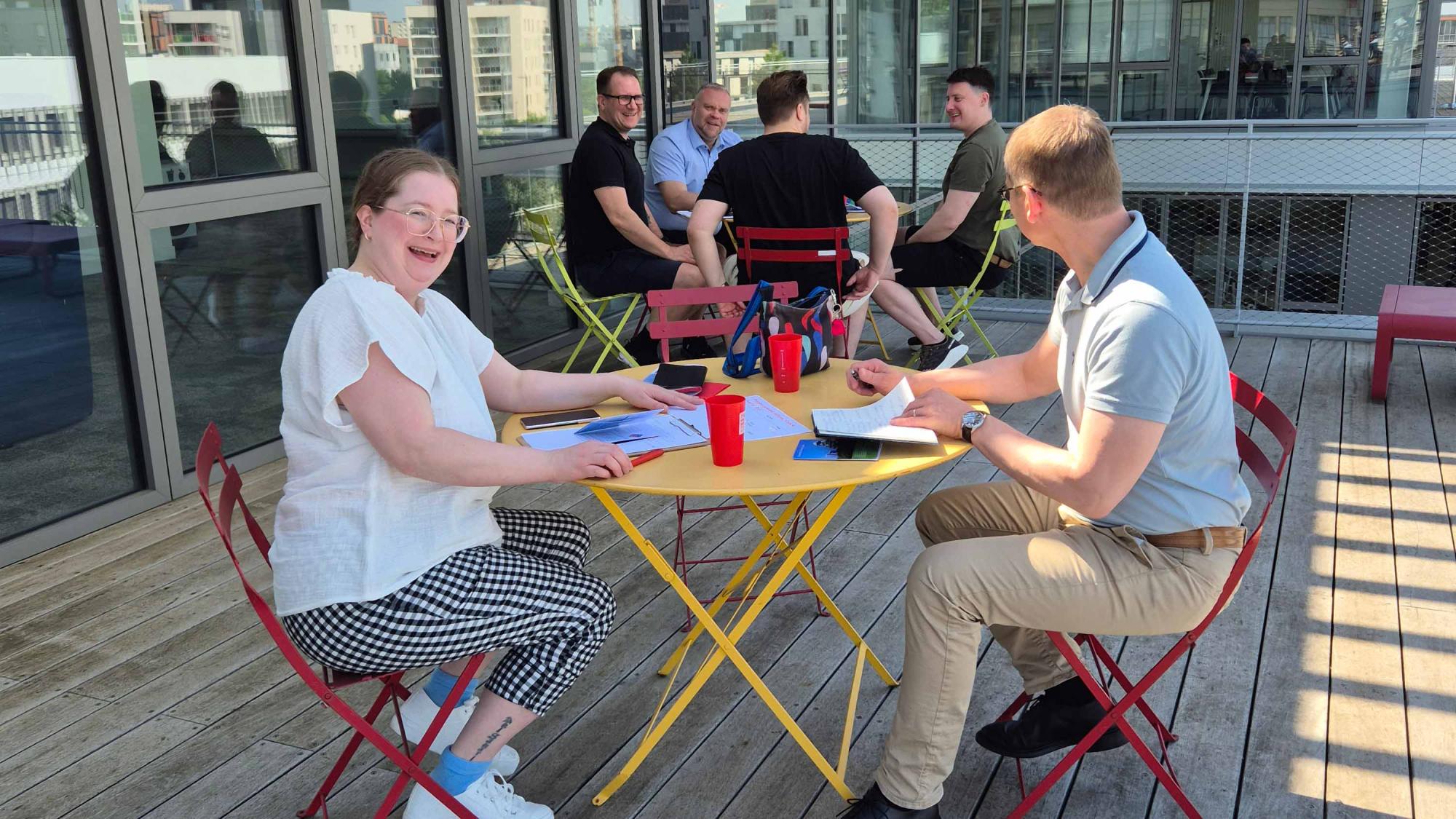 People sitting outdoors at two tables doing groupwork.