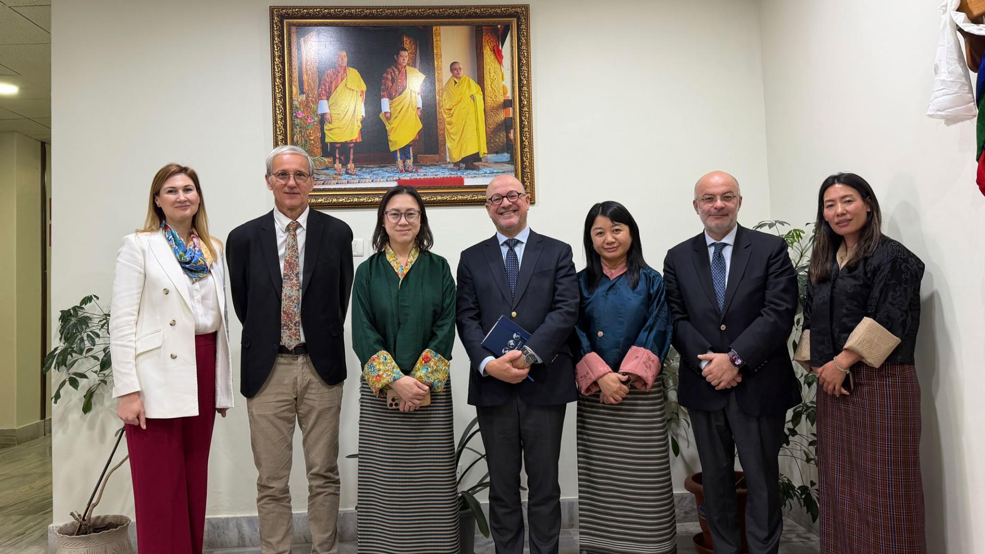 Seven meeting participants standing in line in front of a colorful painting.