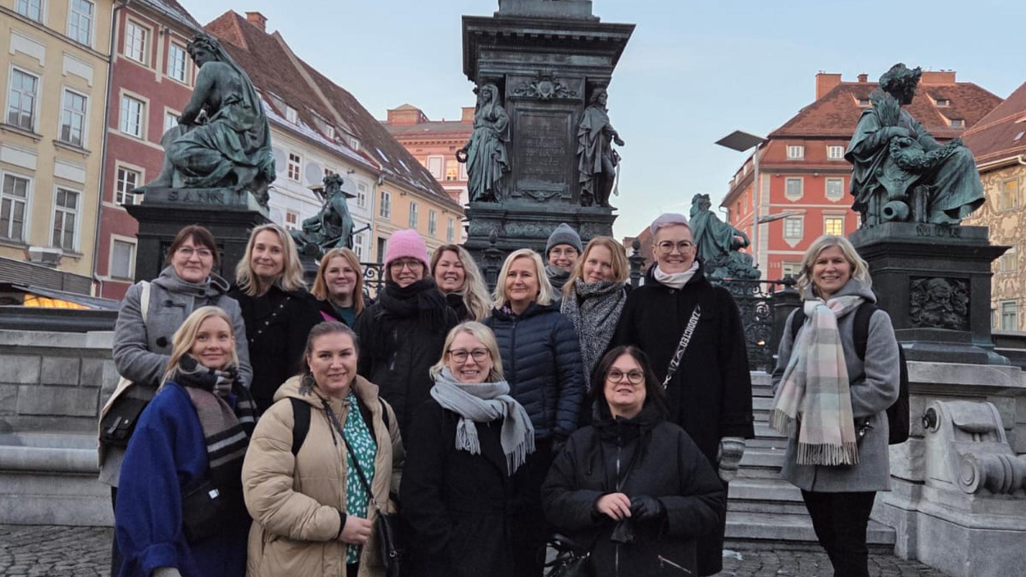 Opiskelijat ryhmäkuvassa, taustalla Grazin kaupungin taloja ja patsaita