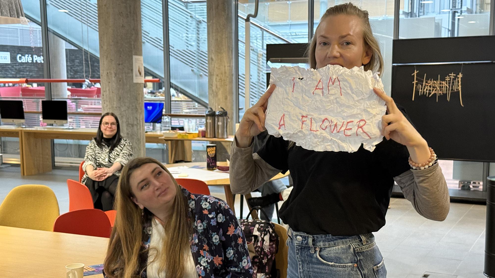 nainen pitelee paperia, jossa lukee "I am a flower"