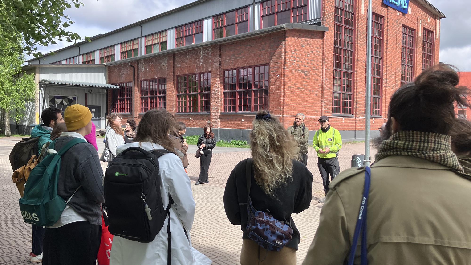 ihmisiä ringissä punatiilisen rakennuksen edessä