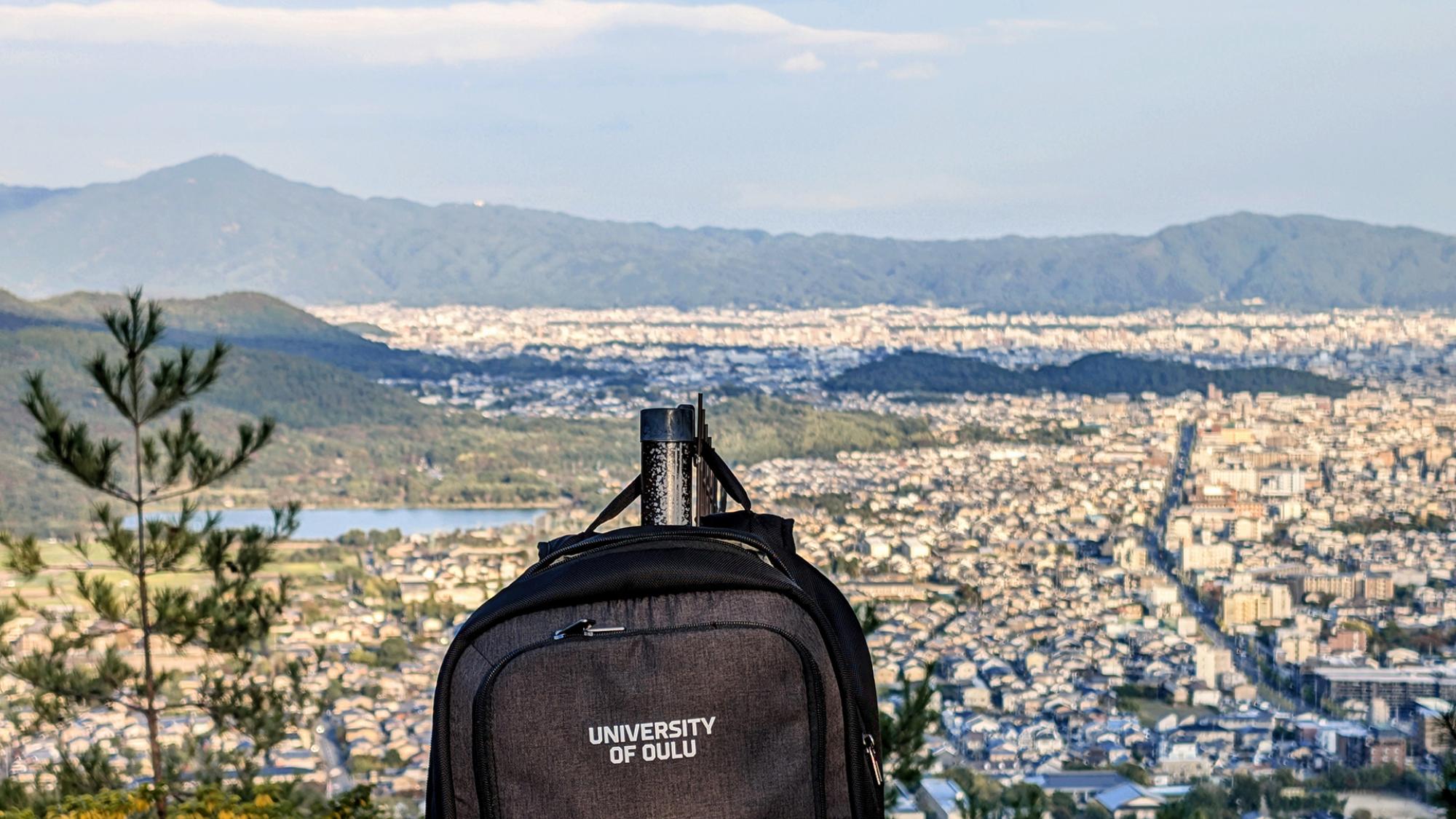Landscape with houses, lake and mountains, with University of Oulu backpack in the foreground