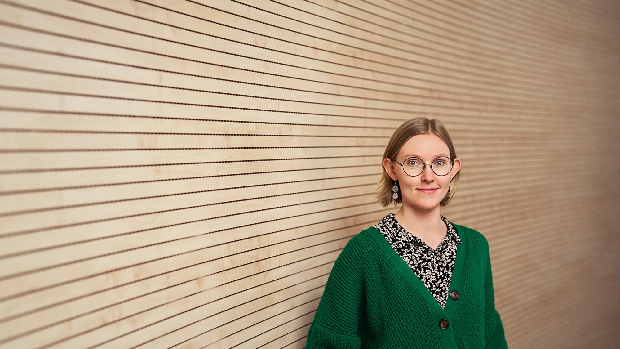 Tutkijaprofiilikuvassa Joula Siponen neutraalin puupaneeliseinän edessä.