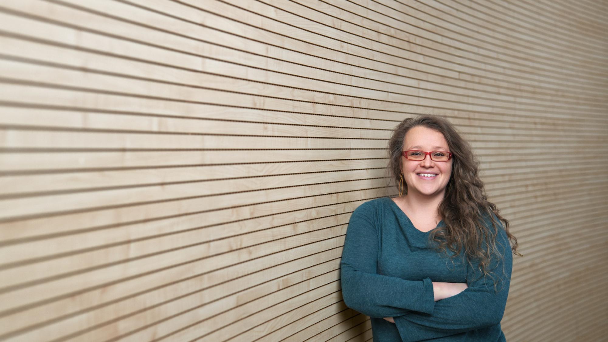 A portrait of Bailey Ashton Adie smiling with a wooden wall in the background