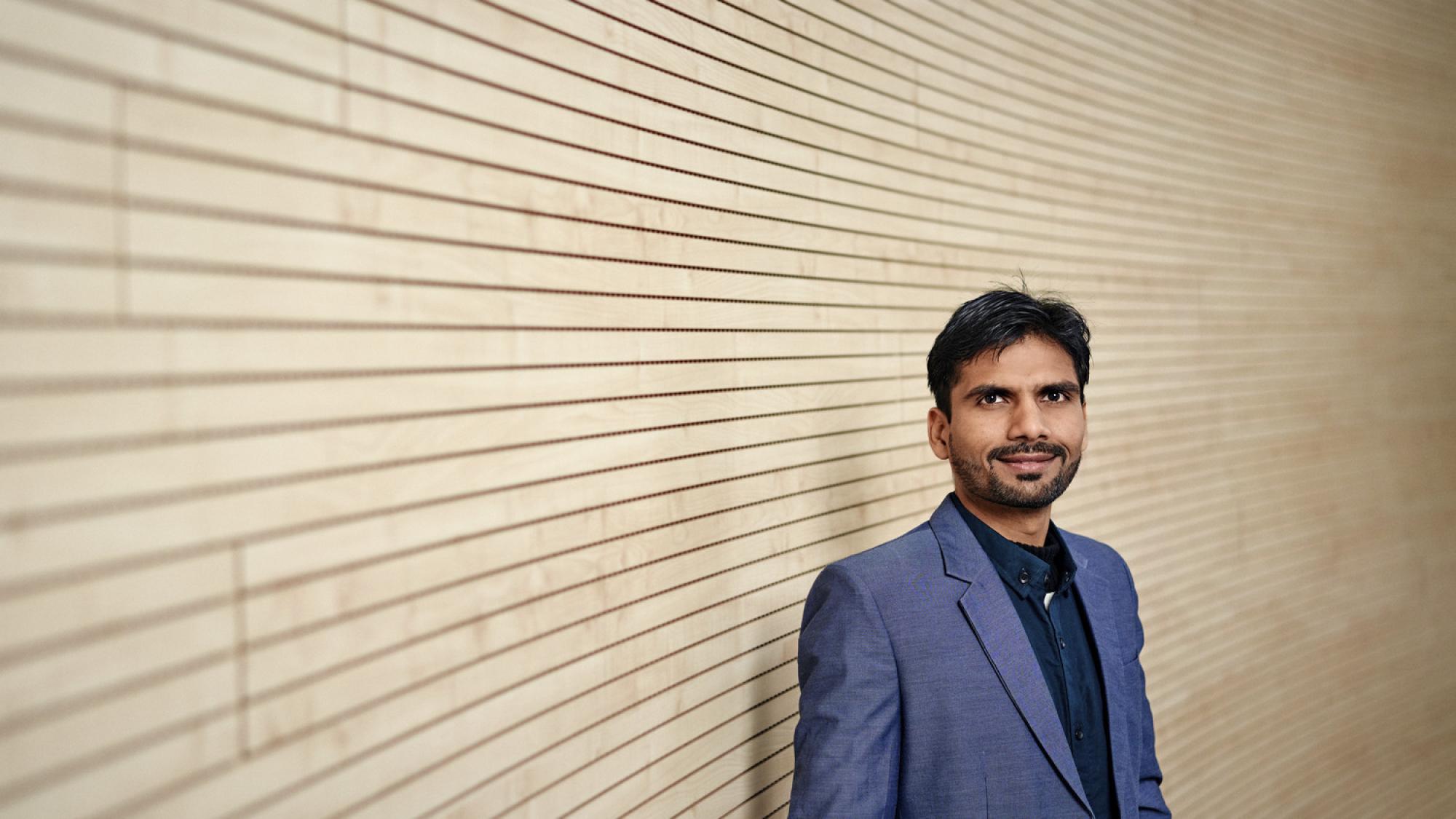 Researcher Saqib Amin in front of a wooden wall.