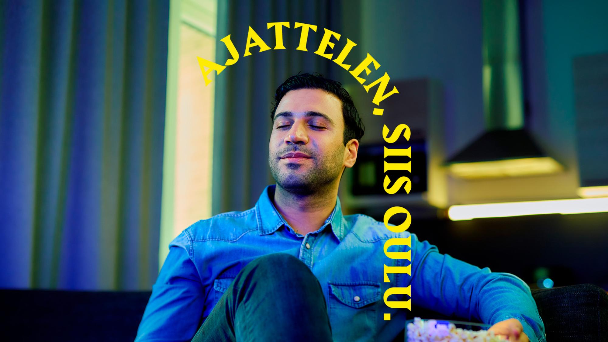 Tummahiuksinen mies istuu silmät kiinni sohvalla. Hänen takanaan on keittiö. Päähenkilön yläpuolella on keltainen kaari, jossa lukee Ajattelen, siis Oulu.