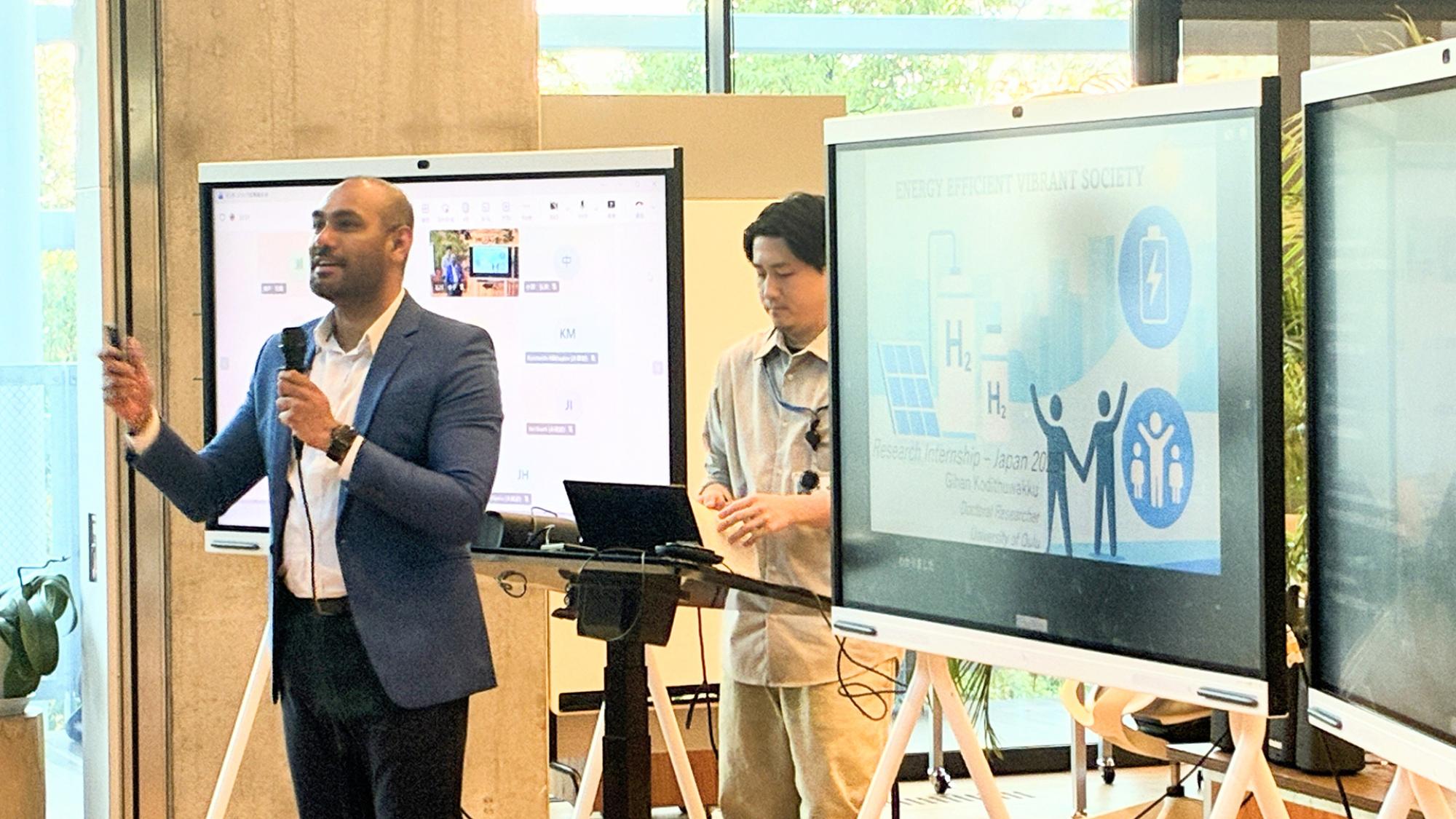 Gihan Kodithuwakku is holding a microphone and there is a presentation on the screen.