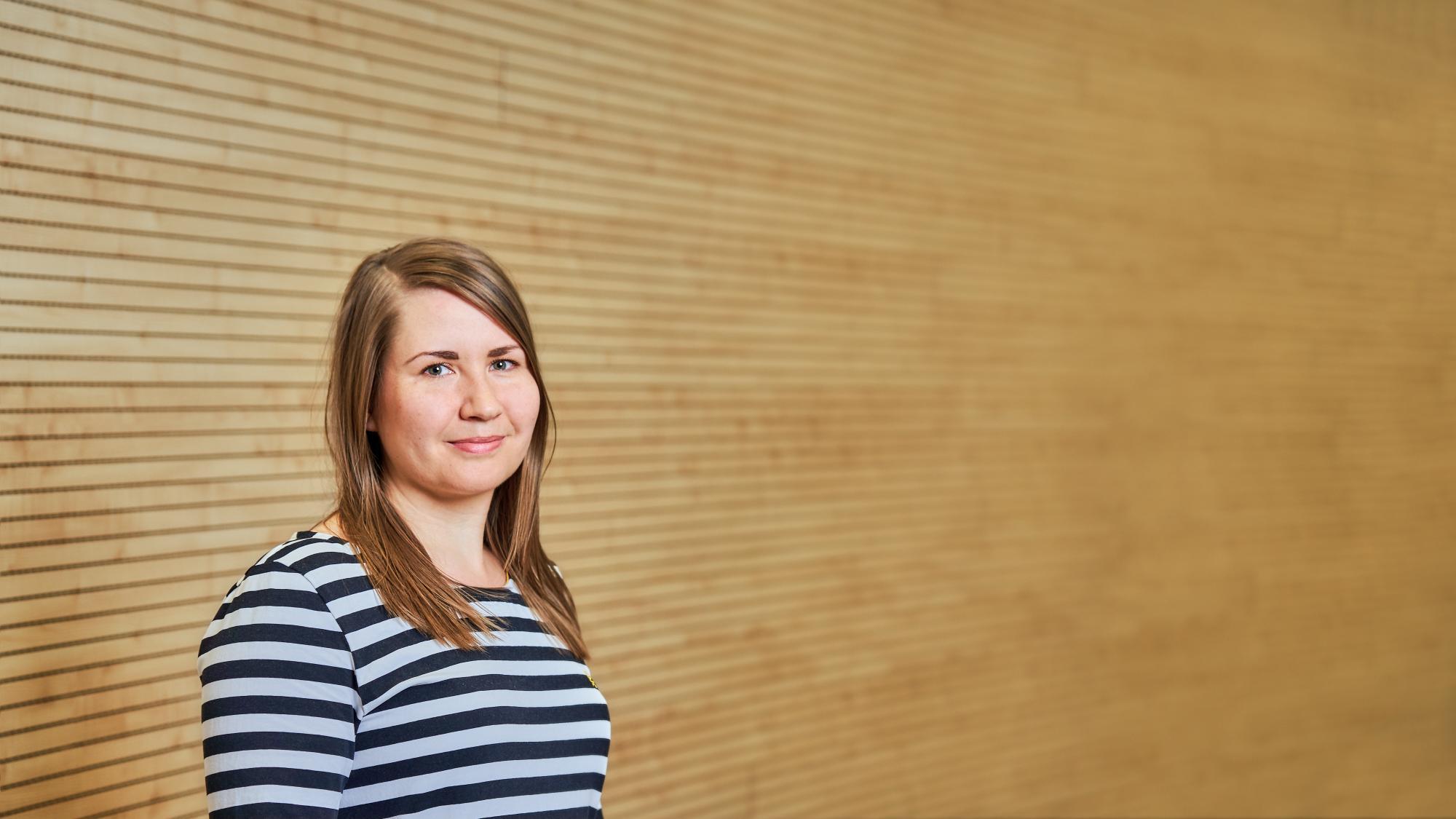 A portrait of researcher Laura Kohonen-Aho with a wooden wall on the background
