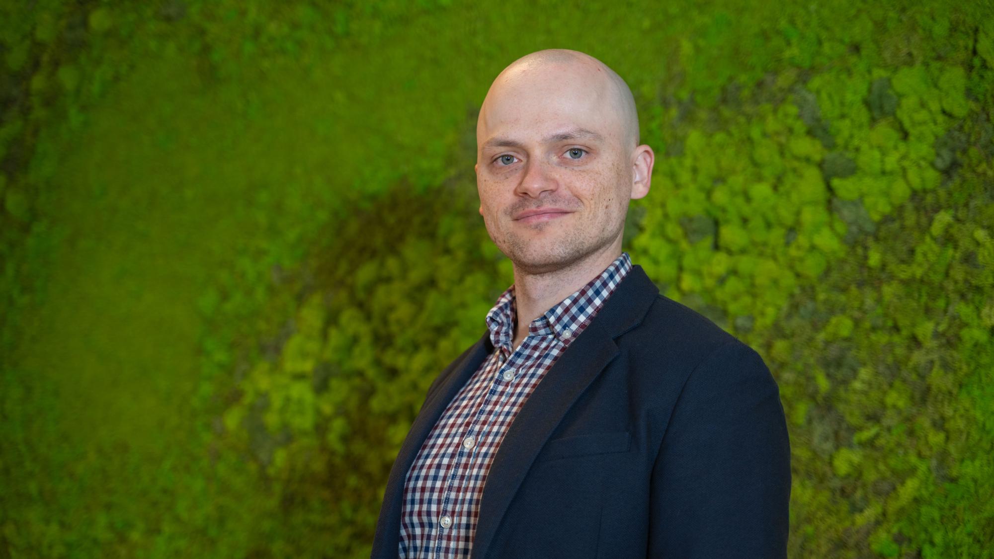 A man standing in front of a green background.
