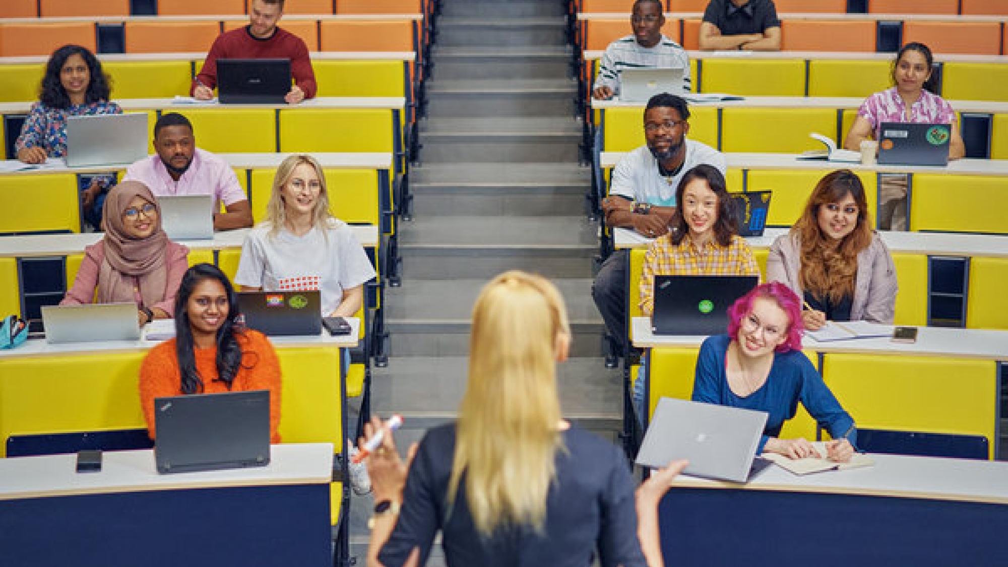 Opettaja opettaa luentosalissa, taustalla opiskelijoita