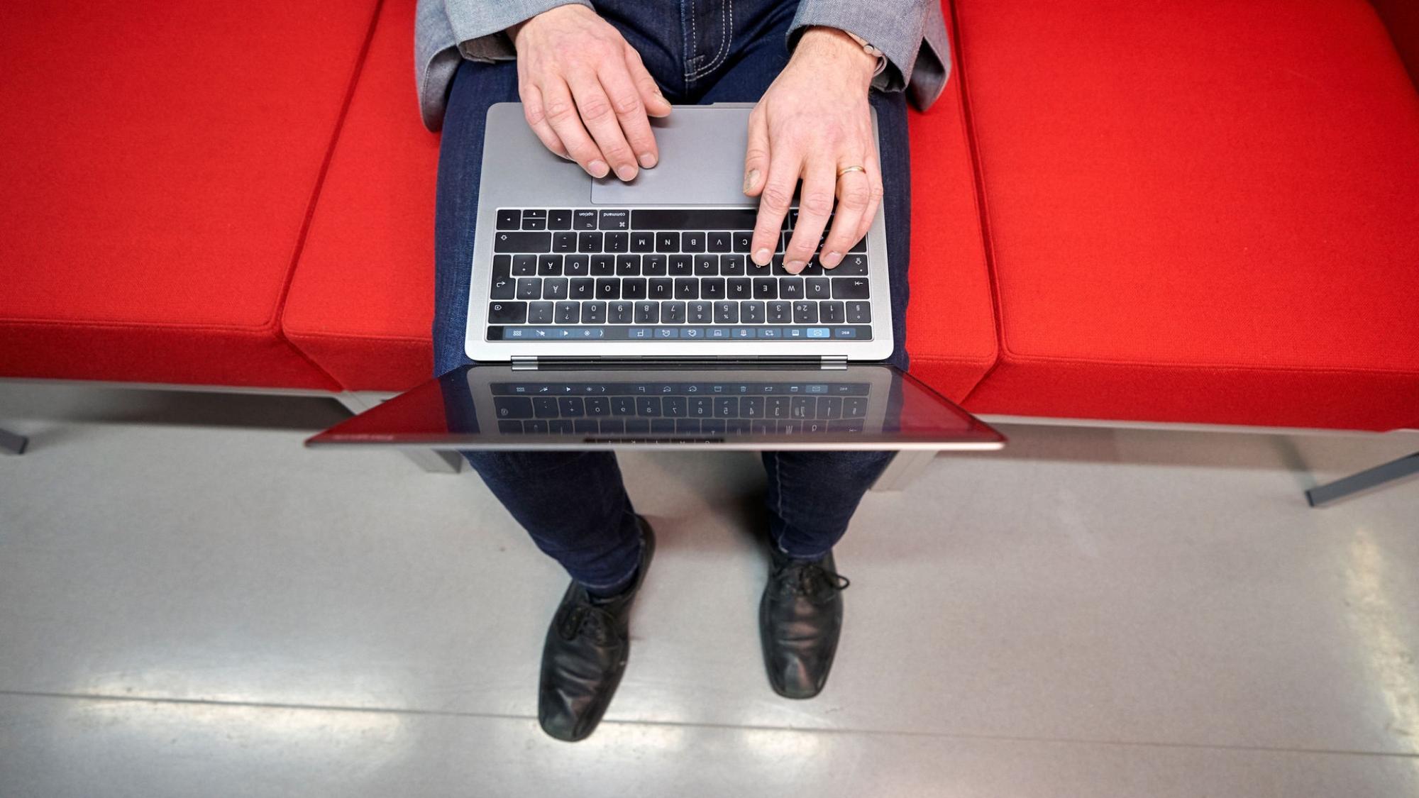 A person sitting on a red couch with a laptop.