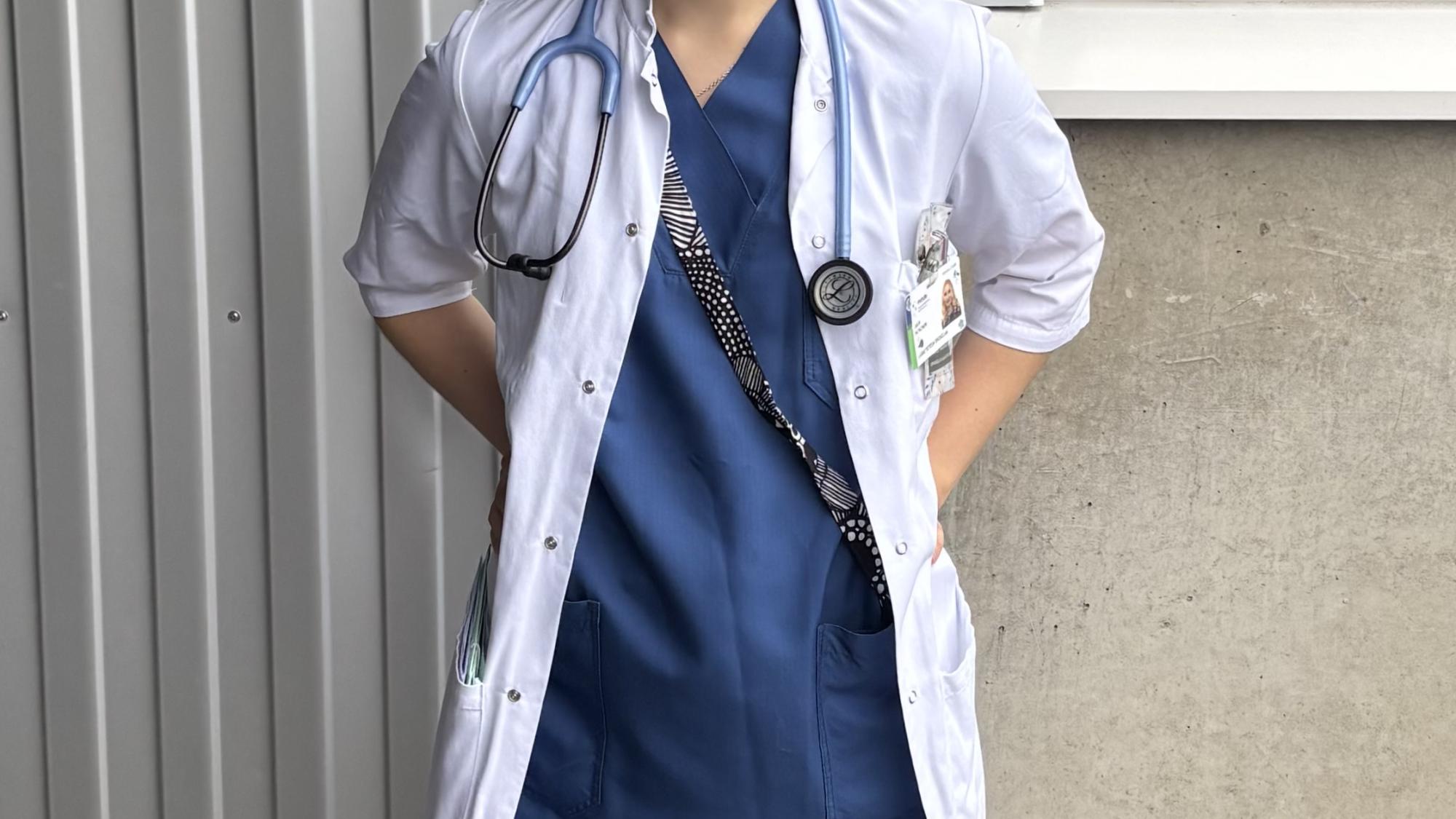 Hymyilevä nainen lääkärintakissa. Kaulassa roikkuu stetoskooppi.