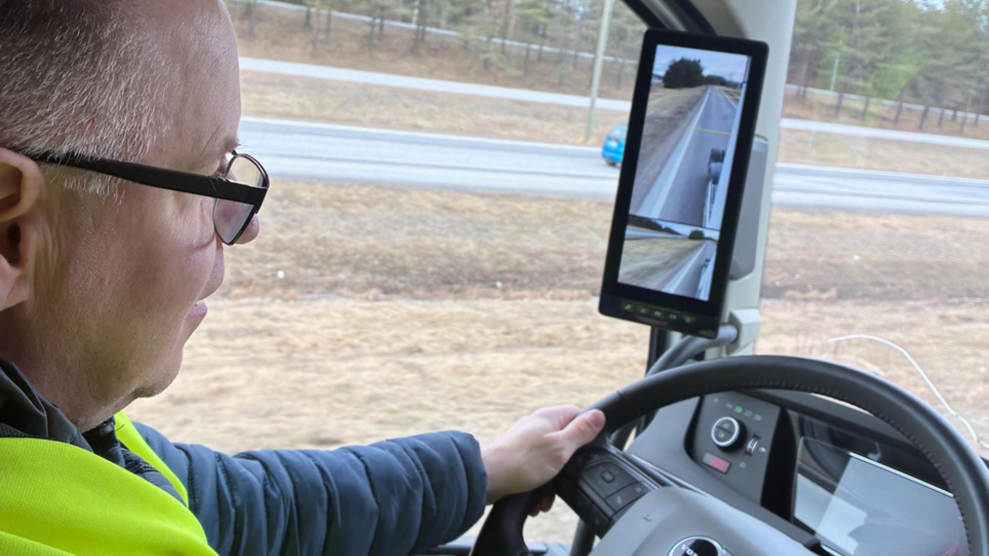 A man holding on a steering wheel when driving a truck on a road.