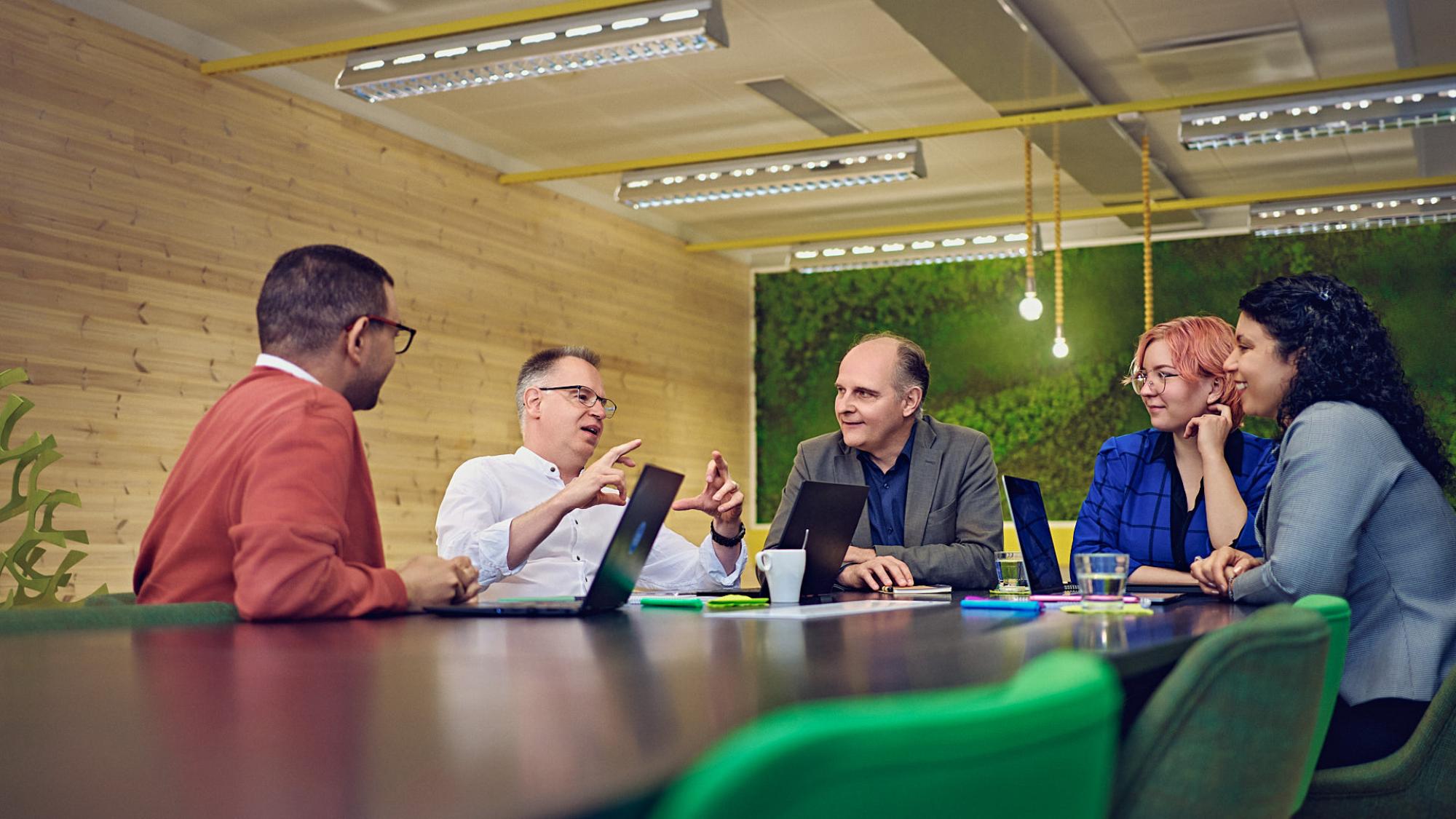 Five people sitting at the end of a meeting room table and discussing.