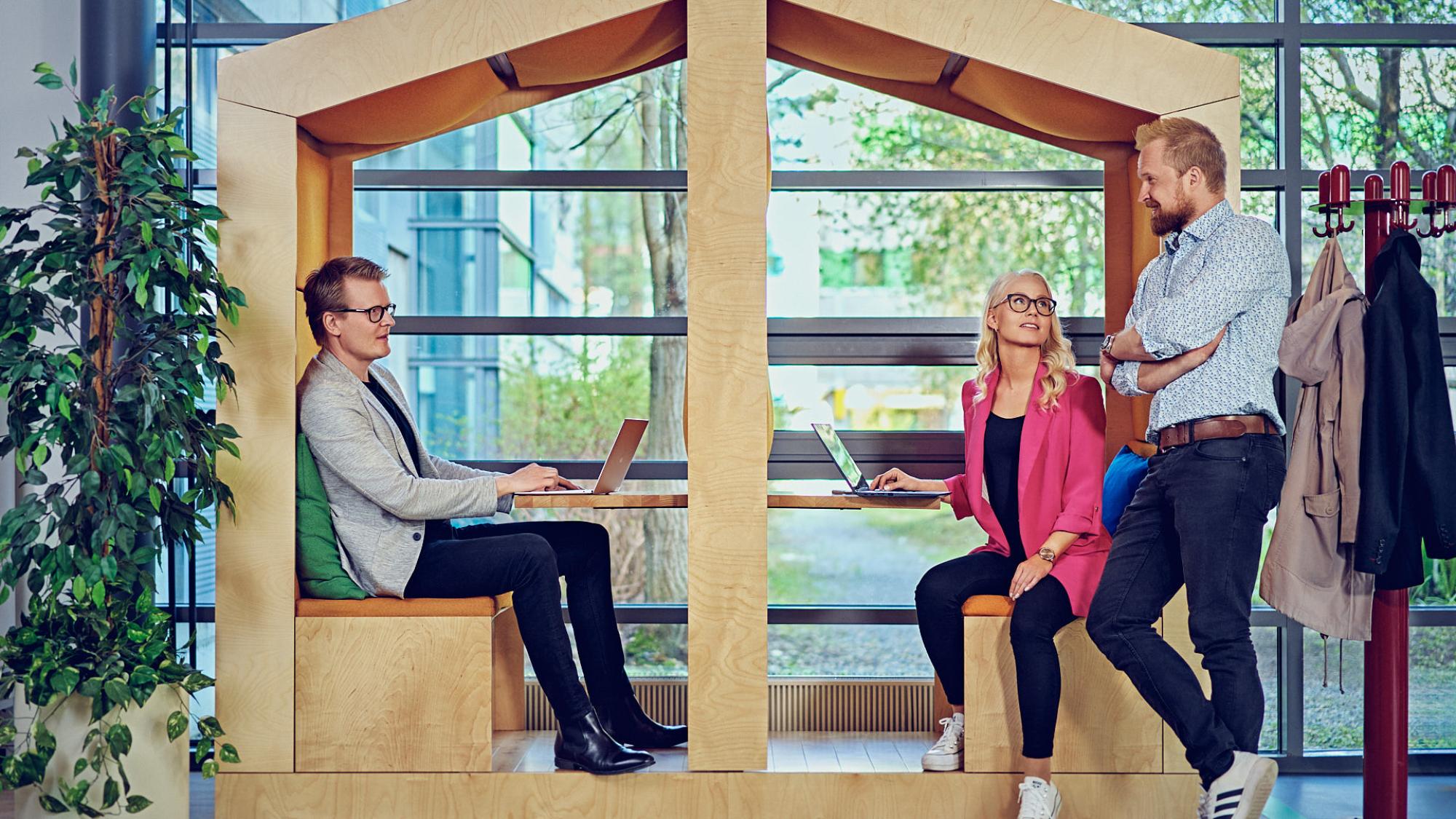Three people discussing in a relaxed setting in front of a glasswall giving towards a yard with with trees.
