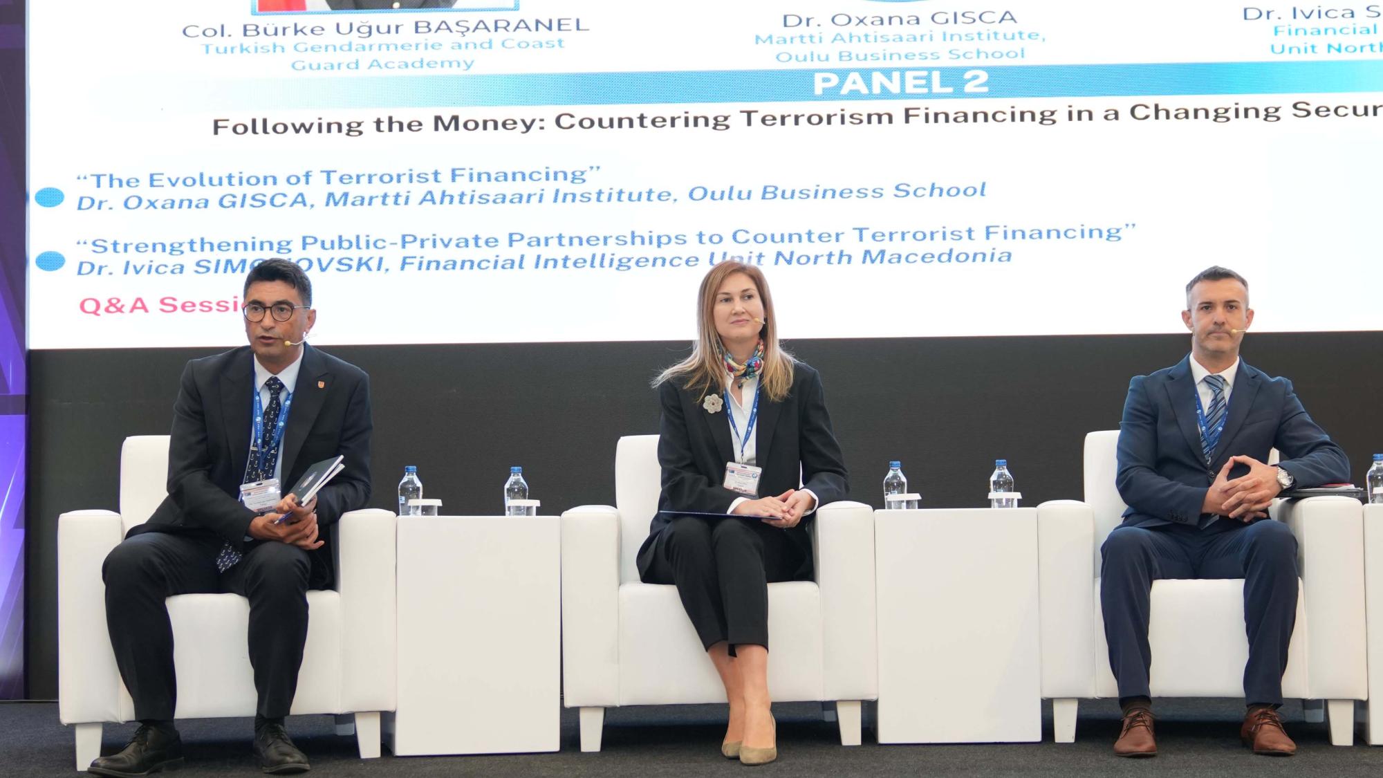 Three smartly dressed people sitting on white armchairs in front of a screen at a panel discussion.