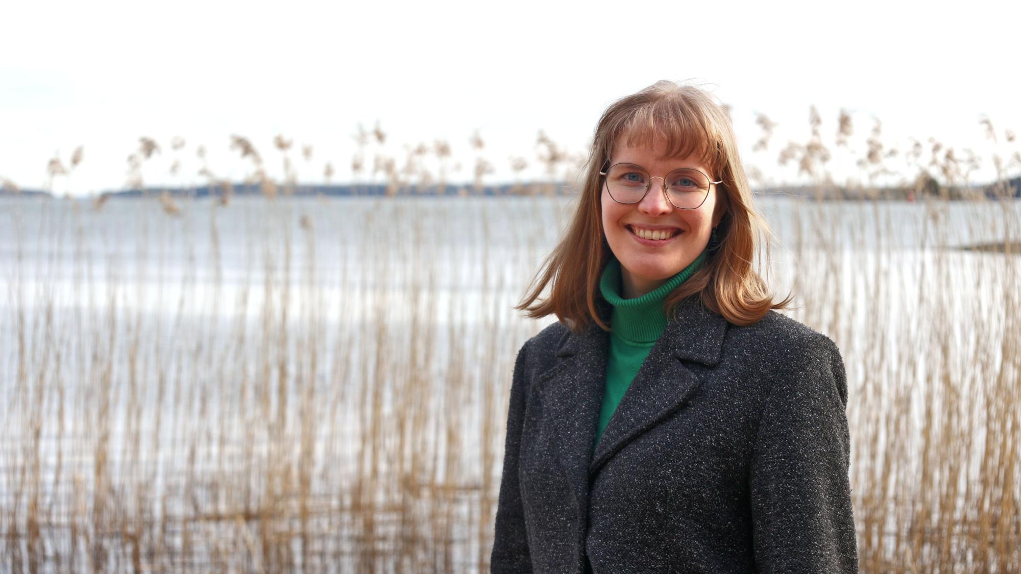 A young woman smiling outside in mild winter weather with sea shore showingin the background