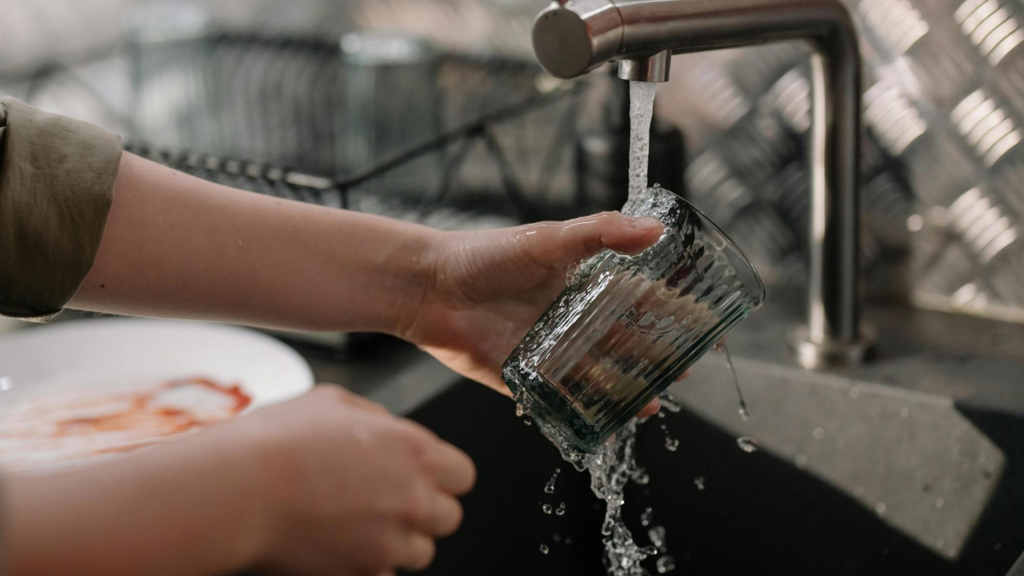 kädet pitelevät vesilasia vesihanan alla