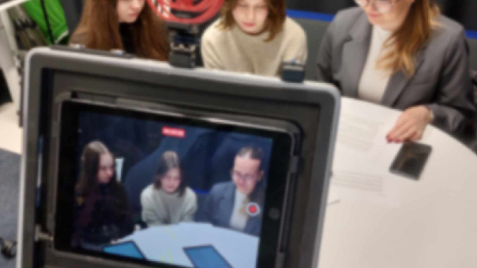 kolme opiskelijaa katsoo yhdessä tablettia ja heitä videoidaan