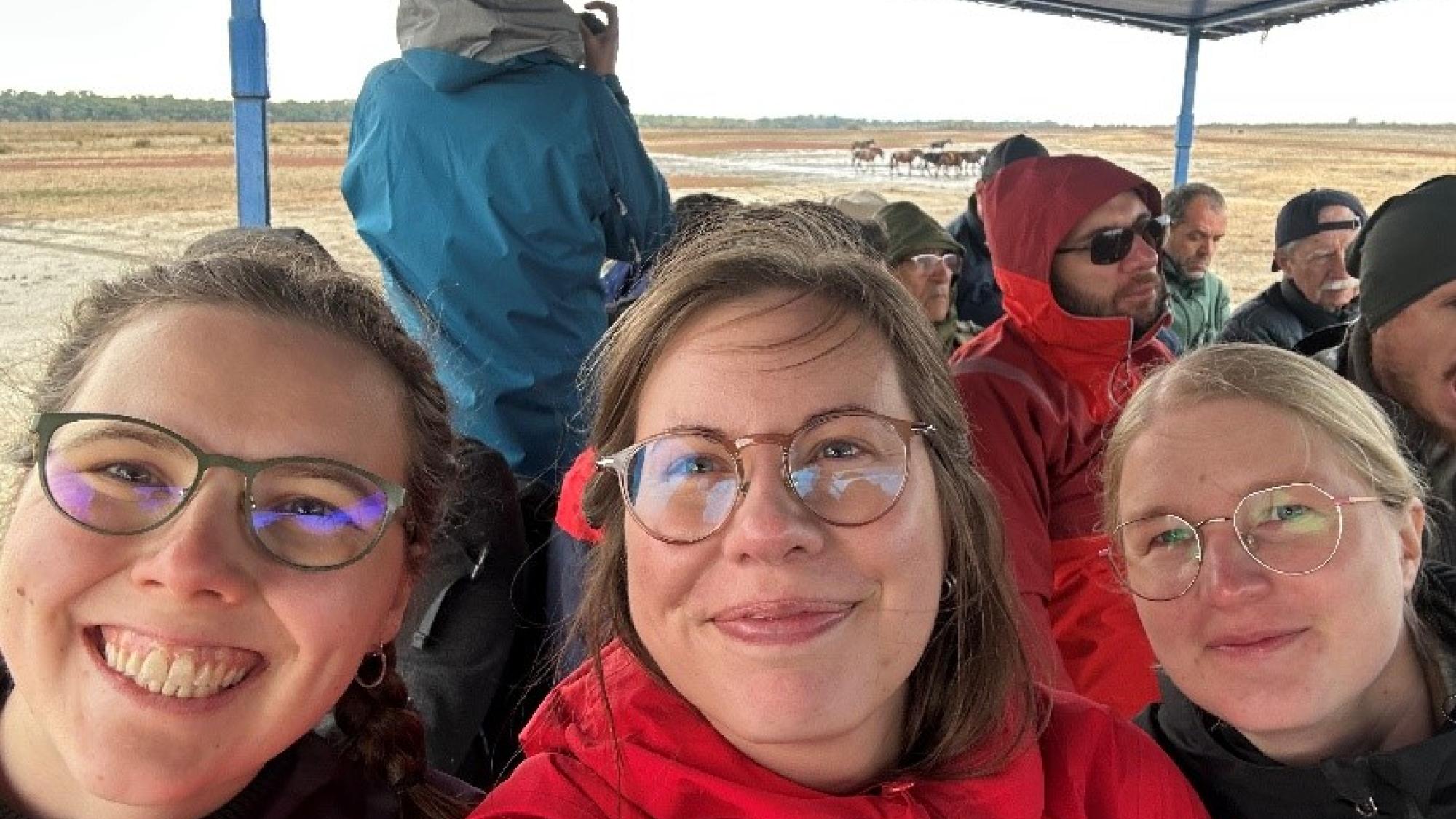 Three woman smiling on a tour outside with other group on the background